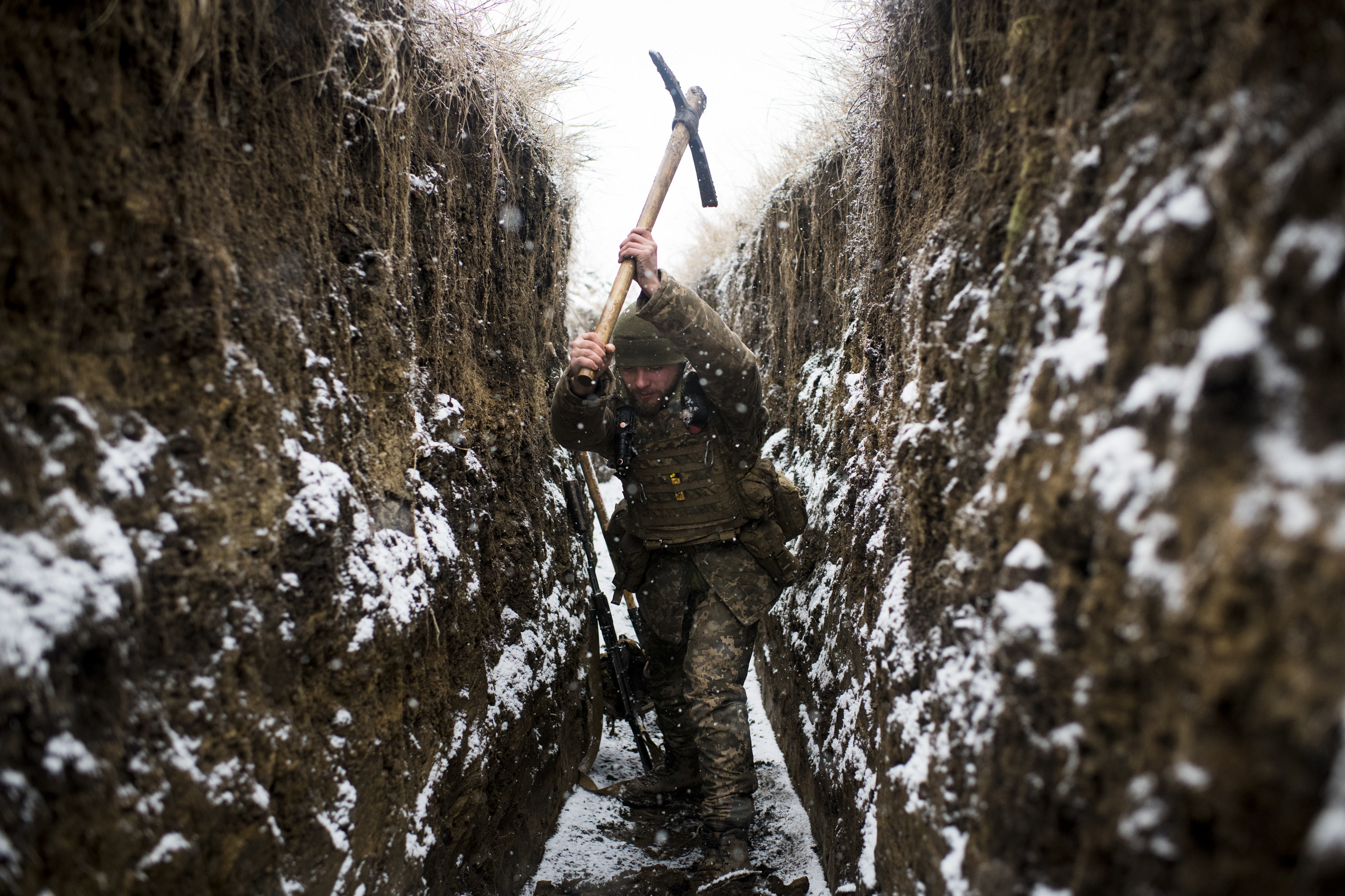 A soldier using a pickax to dig a trench in the snow