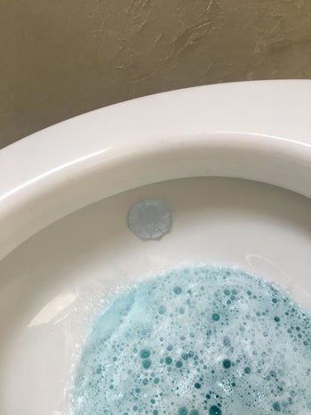 blue gel stamp on side of toilet bowl filled with blue cleaning liquid