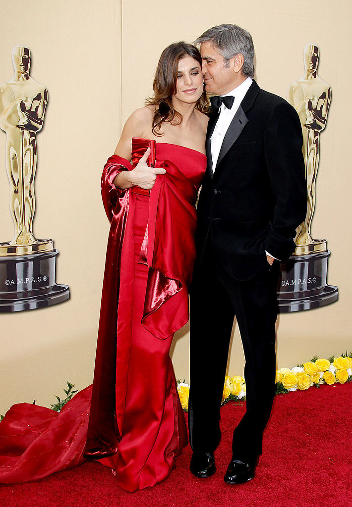 the model wears a long satin gown with a matching wrap and clutch, while the actor wears a classic tux