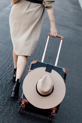 a model rolling a suitcase with the the luggage tag holding a wide-brim hat attached