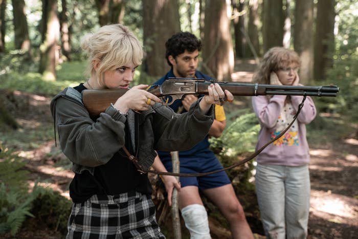 A girl aims a rifle at a target while a girl and an adult man stand close to her