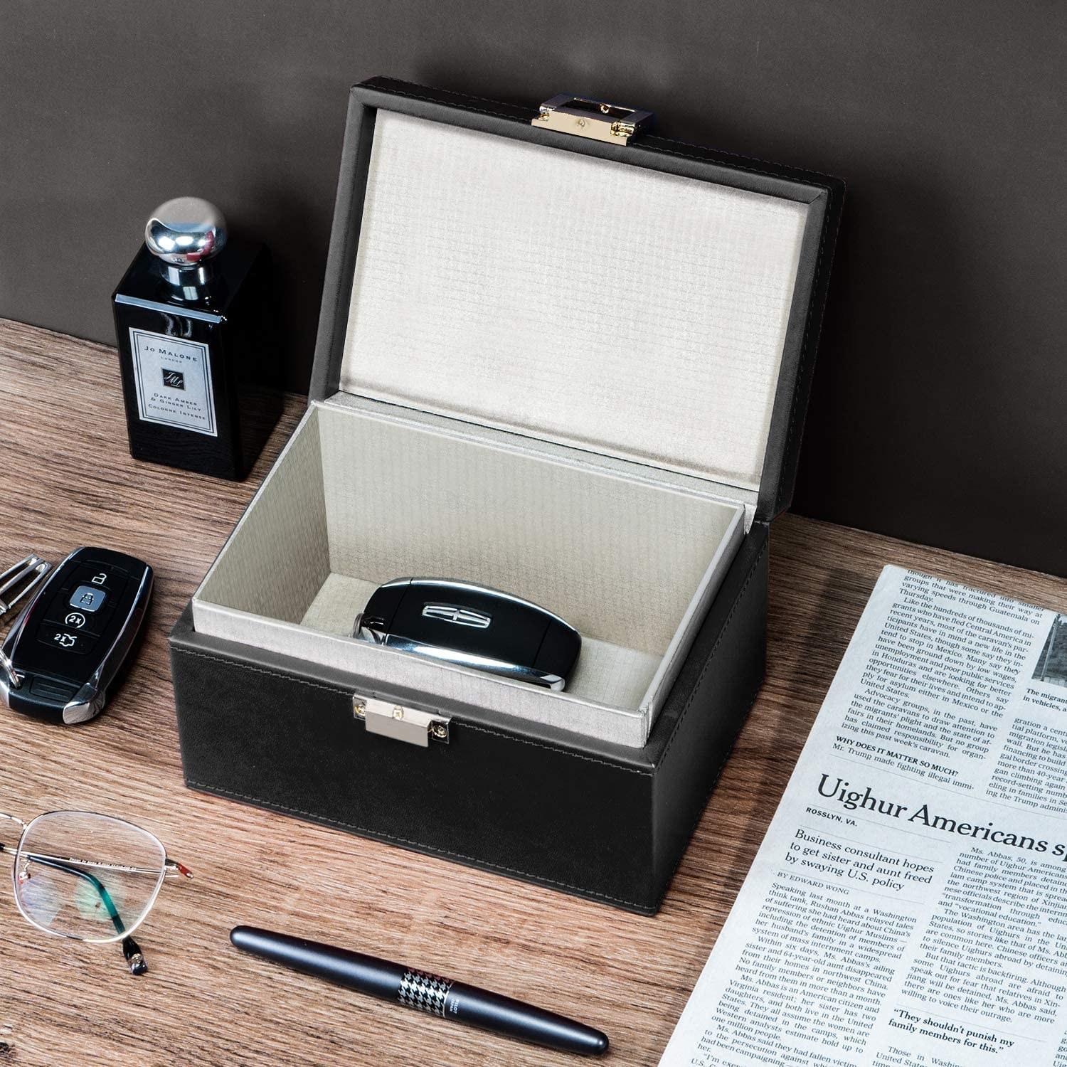 The box open on a table with a key fob inside of it, and various items like glasses and a newspaper surrounding it