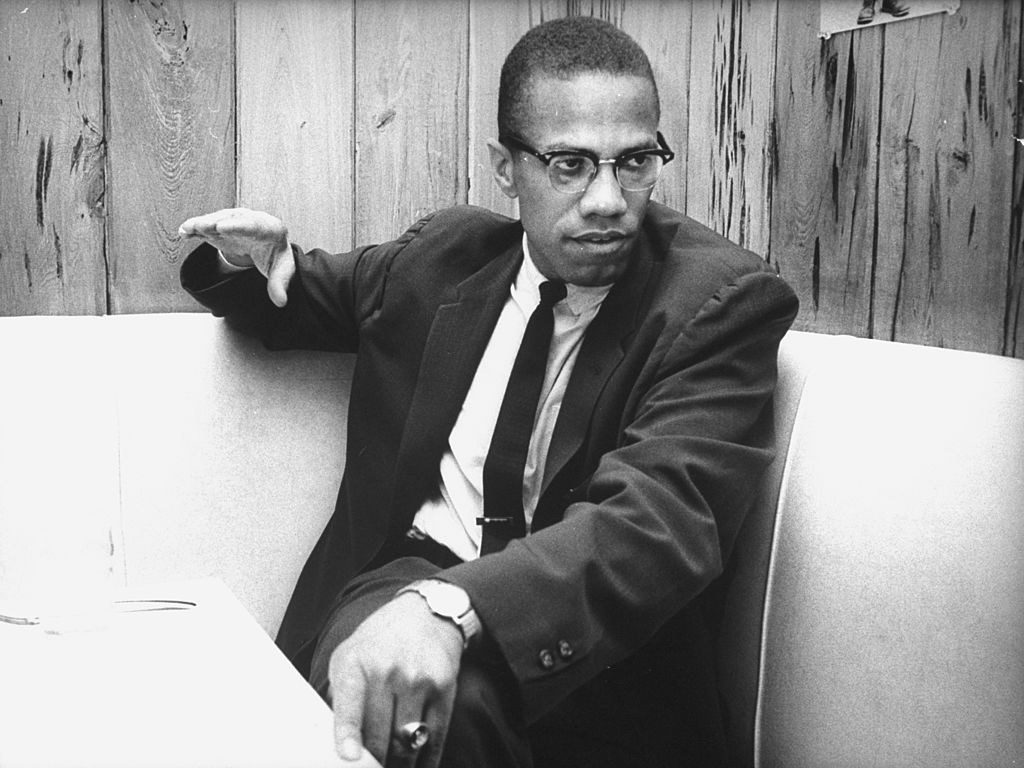 Malcom X sits in a chair.