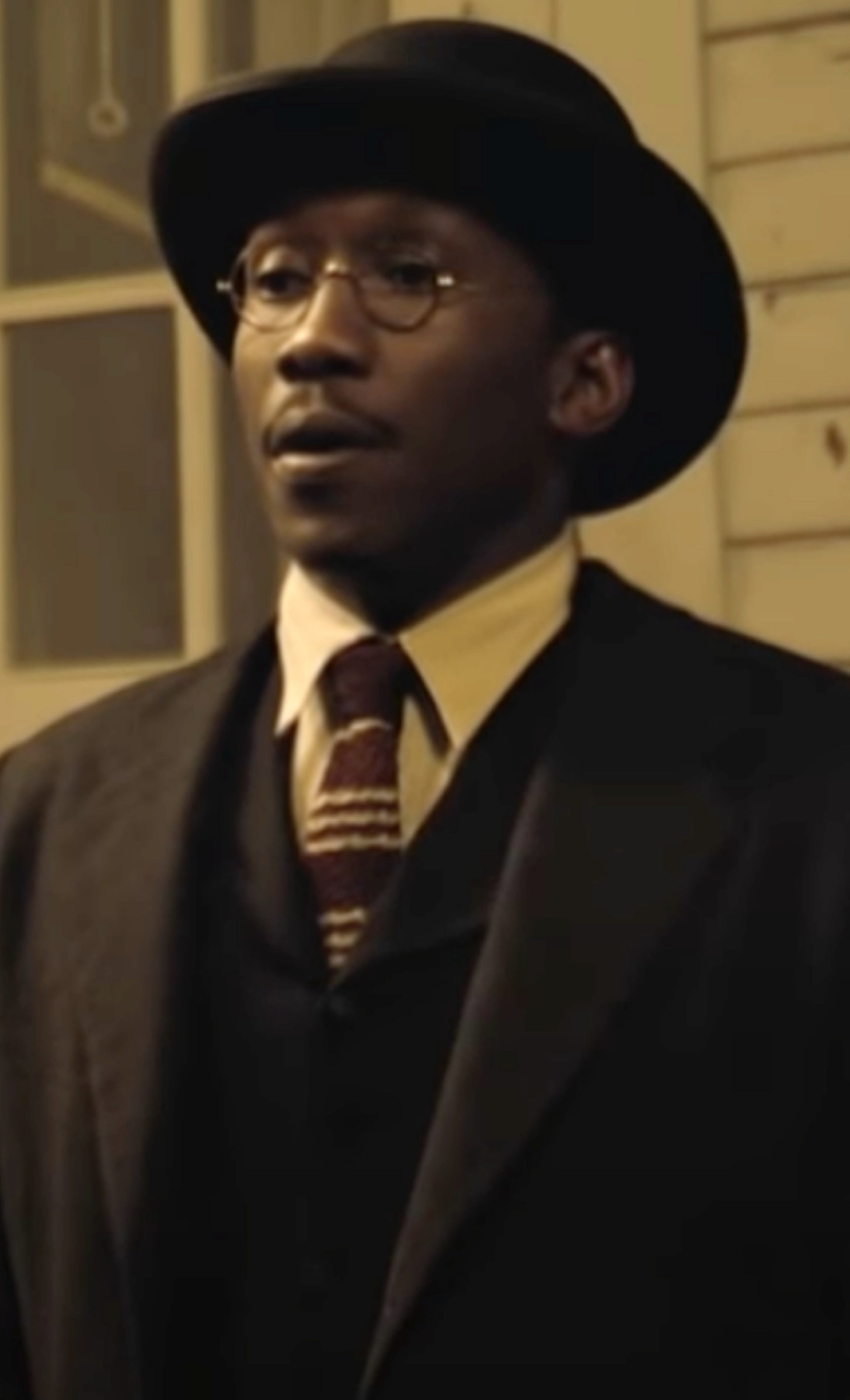 Ali wearing a hat, glasses, and a suit and tie out on the porch