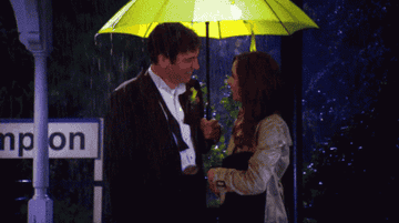 ted and tracy standing under the yellow umbrella in the rain