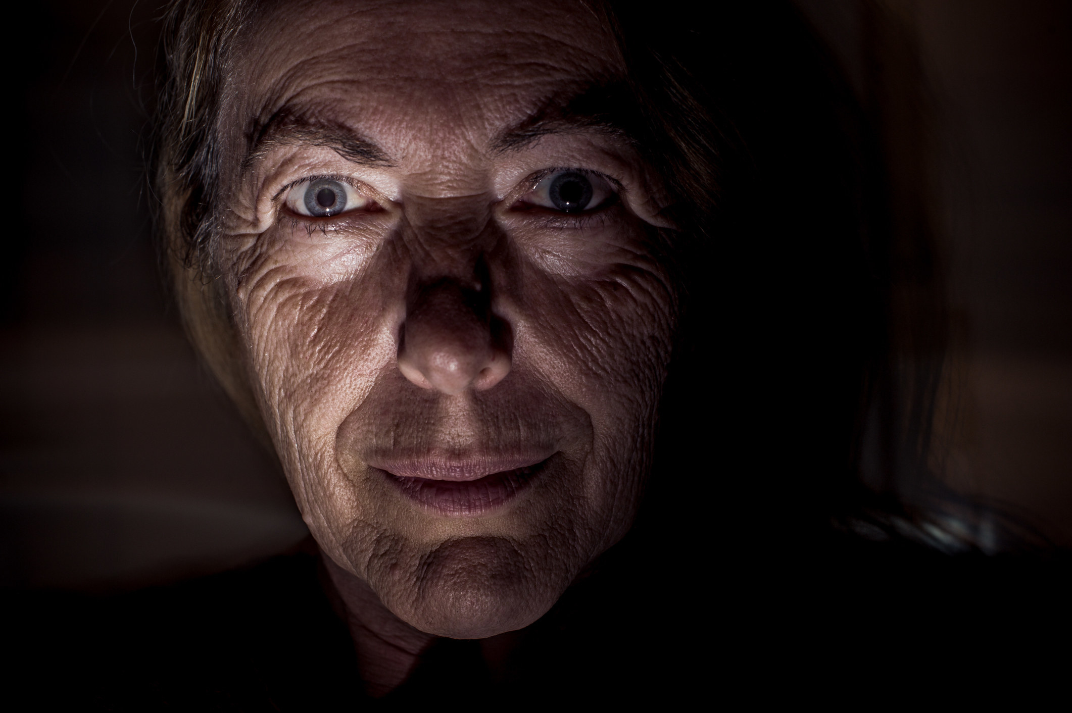 An elderly woman smirks in the dark