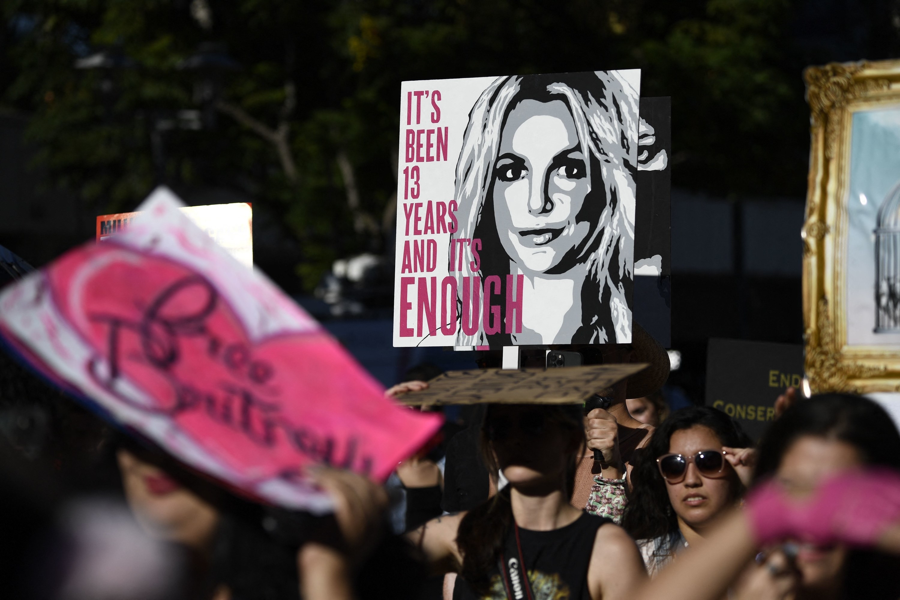 Someone in a crowd of demonstrators holds a sign with a picture of Britney Spears, reading, &quot;It&#x27;s been 13 years and it&#x27;s enough&quot;