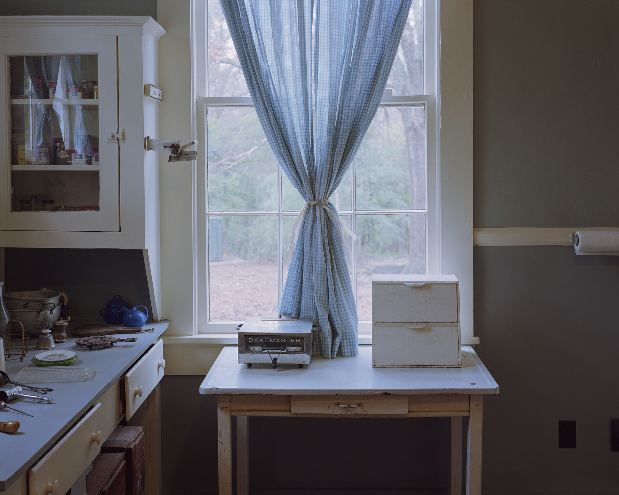 “William Faulkner’s Kitchen Curtains, Rowan Oak, Oxford, Mississippi, 2018”: an interior of a kitchen with curtains tied together
