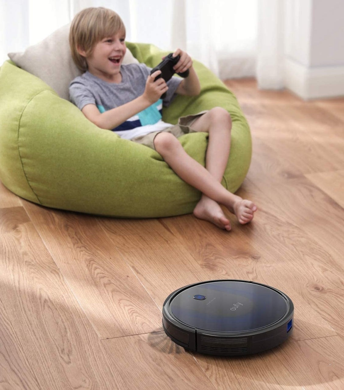 A child sitting in a bean bag chair with a robot vacuum cleaning the floor in front of them