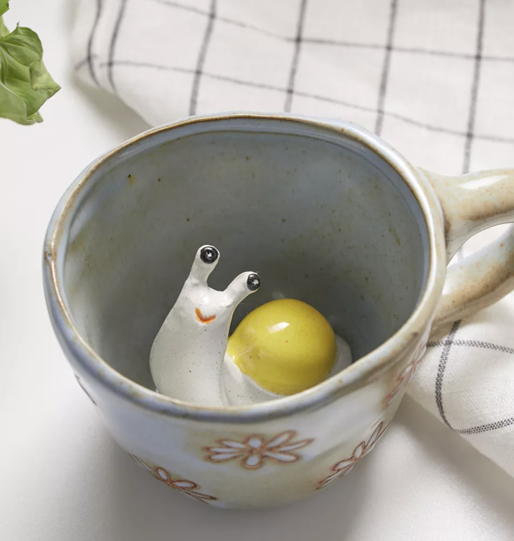 A small white floral mug with a little ceramic snail poking its head out from the bottom
