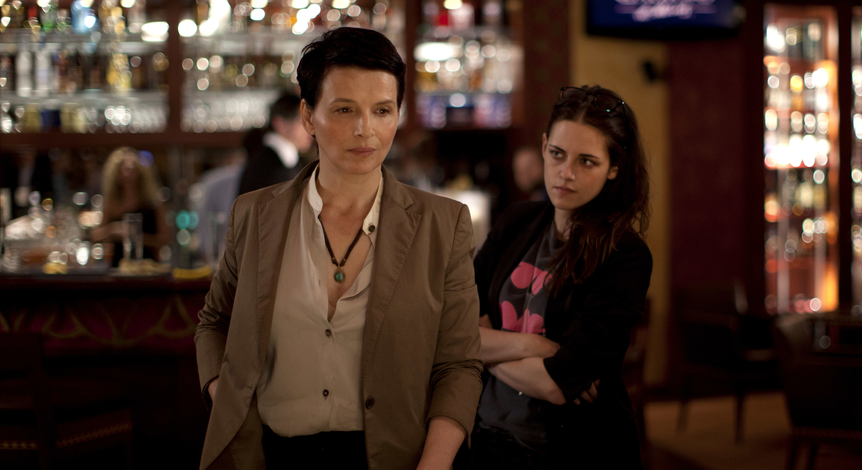 Juliette Binoche and Kristen Stewart stand in a bar
