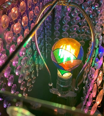 Close-up of a reviewer's multicolored, iridescent light bulb inside a crystal chandelier