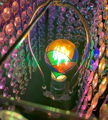 Close-up of a multicolored, iridescent light bulb inside a crystal chandelier