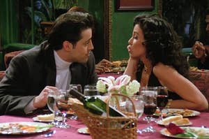 Joey from Friends and his date sitting next to each other at a restaurant with food in front of them