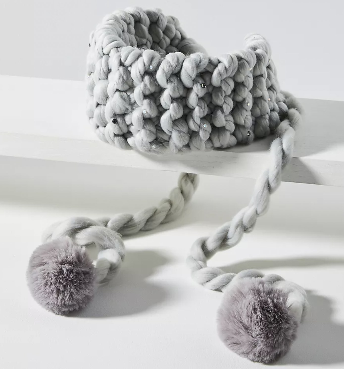 a grey knit ear warmer with rhinestones and pom-poms that tie in the back