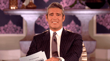 Andy Cohen wearing a pinstriped suit cringing