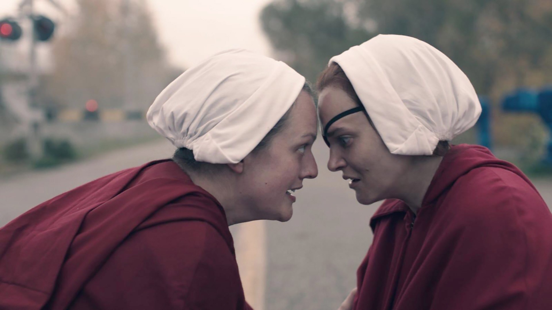 june and janine look each other closely in the eye while wearing their handmaid outfits
