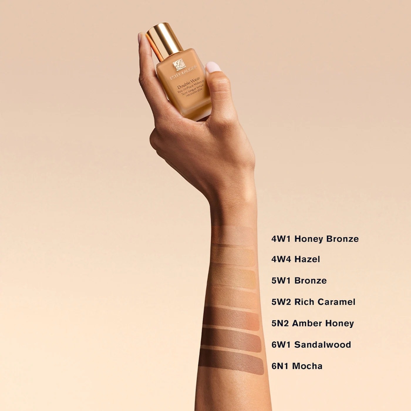 Model&#x27;s hand holding a bottle of foundation with swatches of different foundation shades on their arm