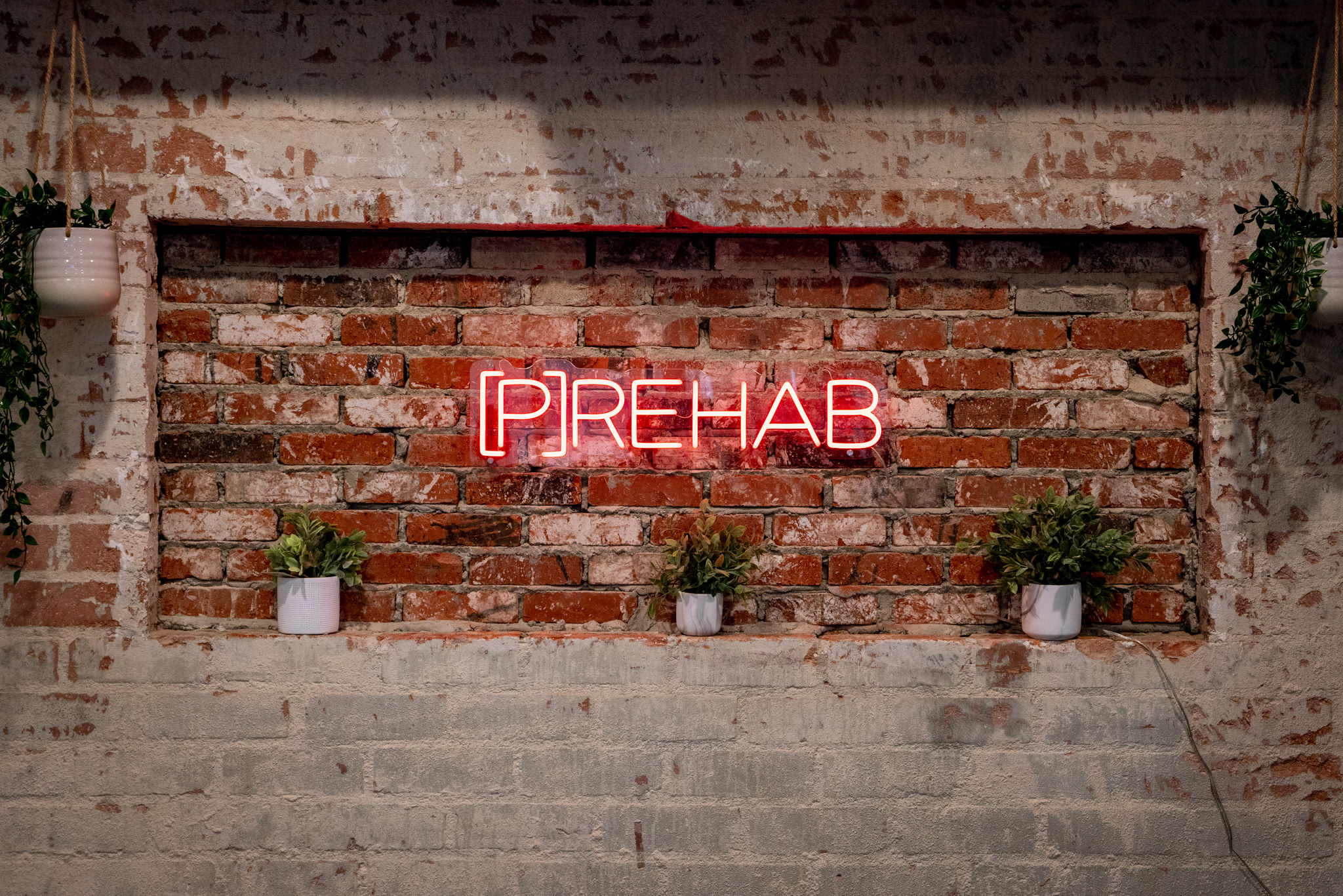 Neon sign of [P]Rehab against an exposed brick interior