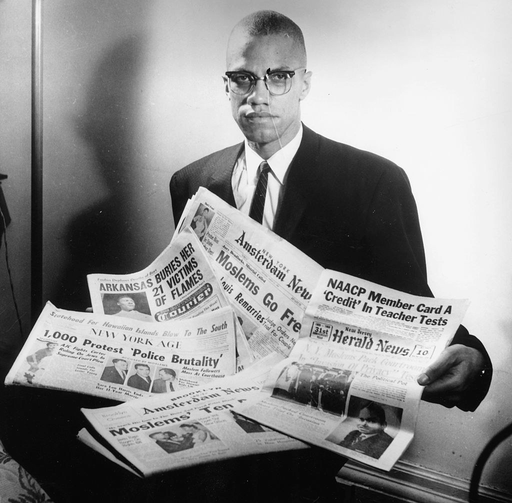 Malcolm X holding a pile of newspapers