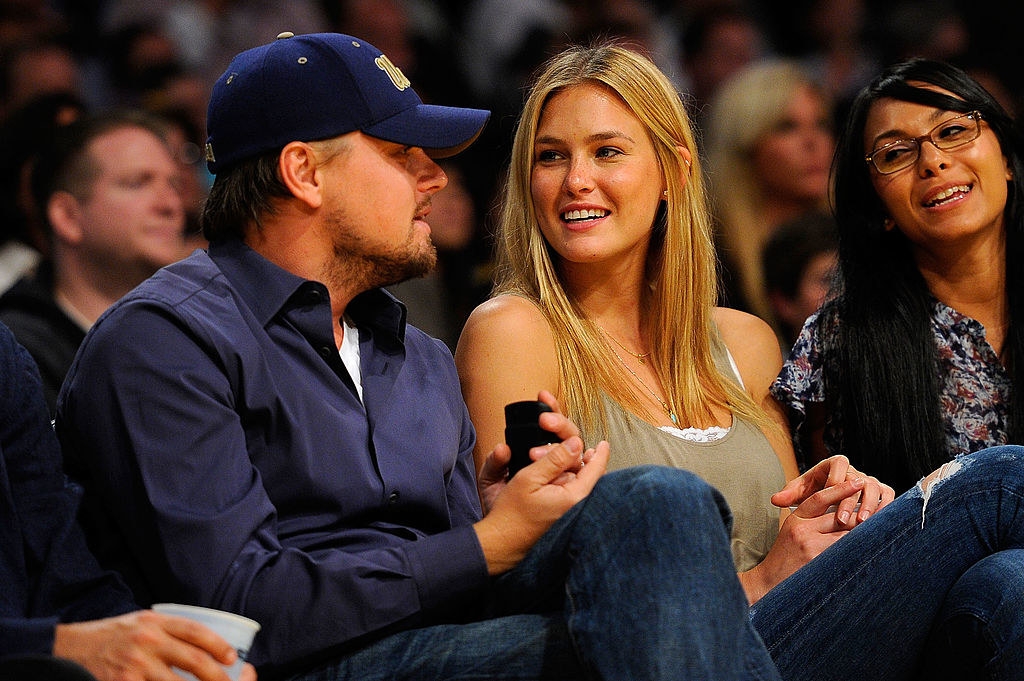 Leo and a blonde woman sitting courtside at a sporting event