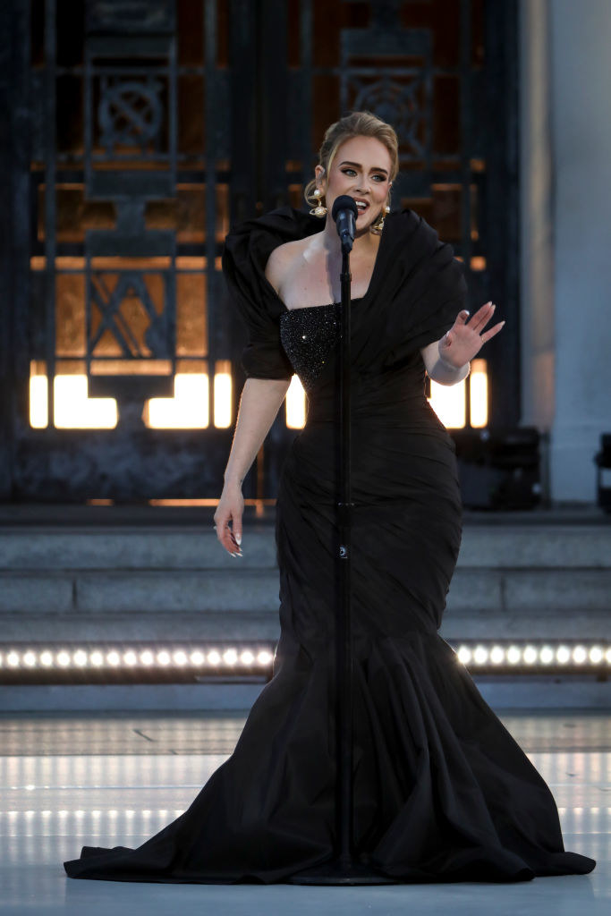 Adele performing onstage at her concert special; she&#x27;s wearing an Old Hollywood–inspired black gown