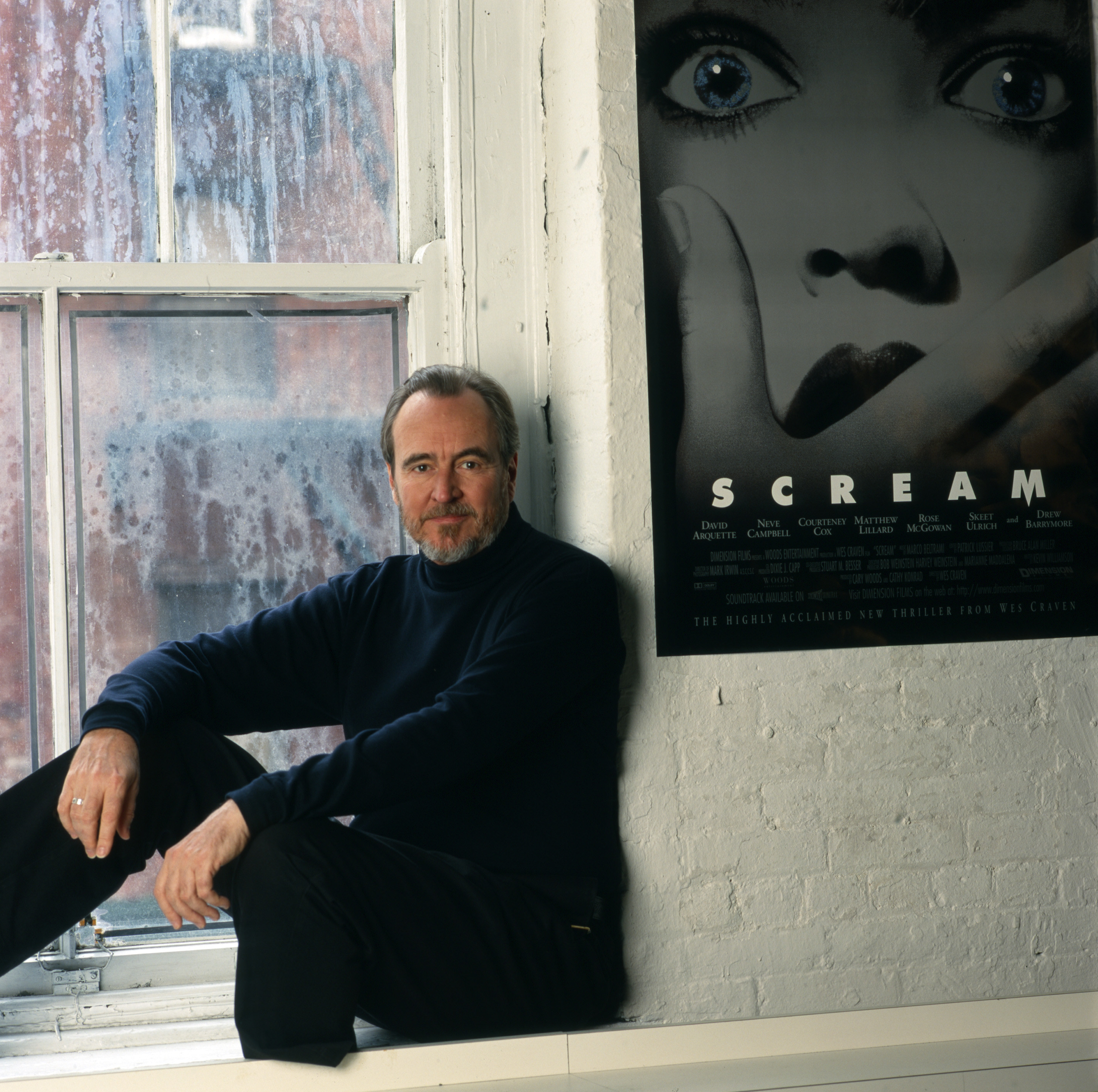 Wes Craven sitting near a Scream poster