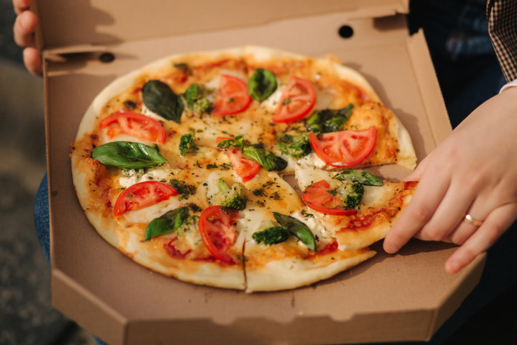 A hand reaching for a slice of a pizza pie in an open box