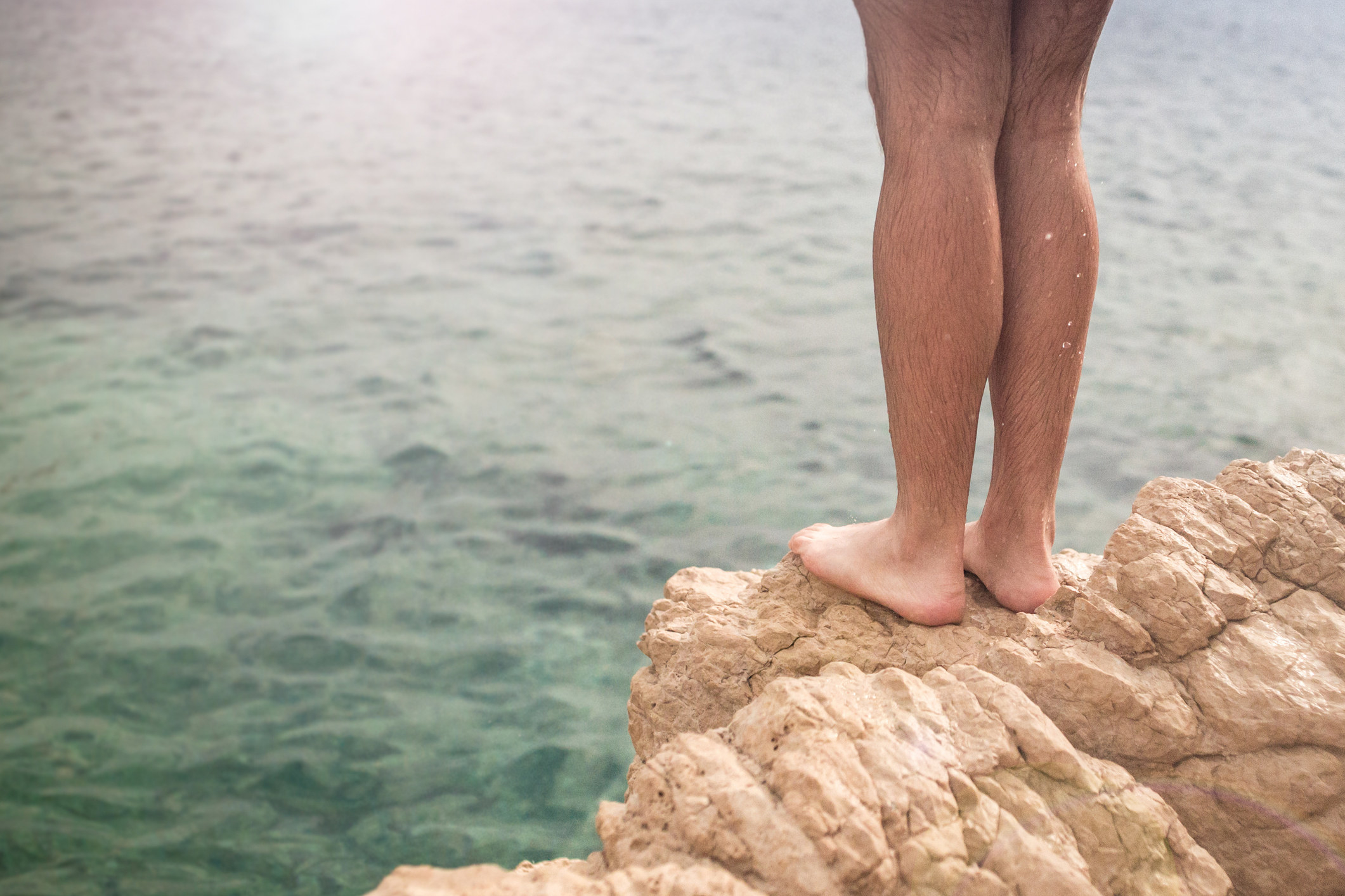 The legs of a person preparing to jump into a body of water off a rocky point
