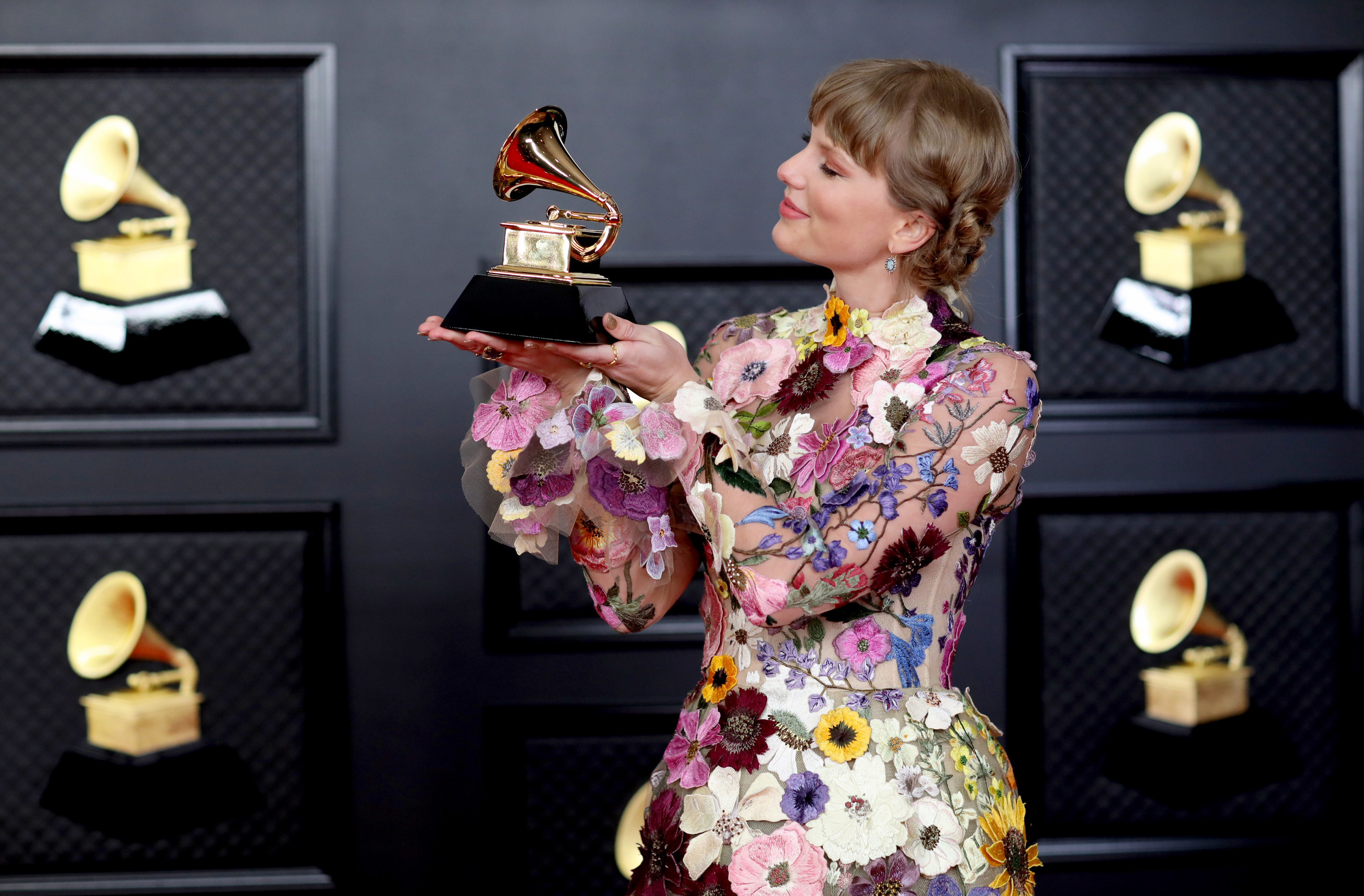 Taylor holding up and smiling at a Grammy she just won