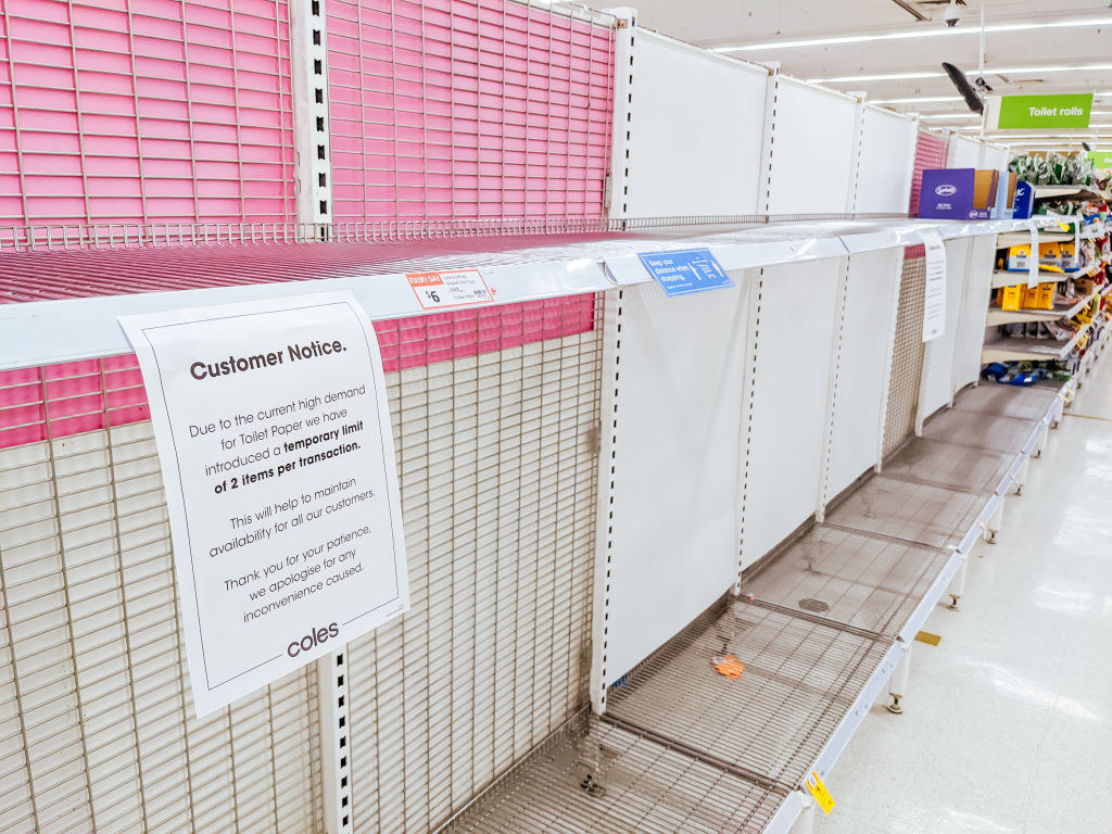 Empty shelves in a grocery store with a sign advising customers that there will be a temporary limit on toilet paper