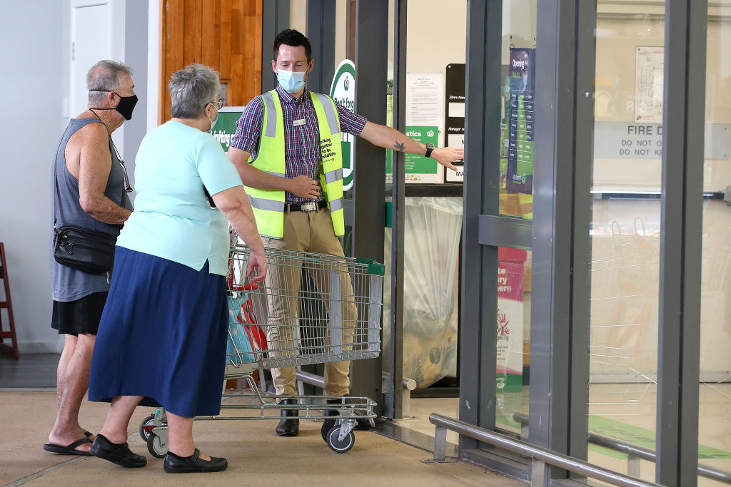 An attendant controls entry as people stand in line outside a Woolworths