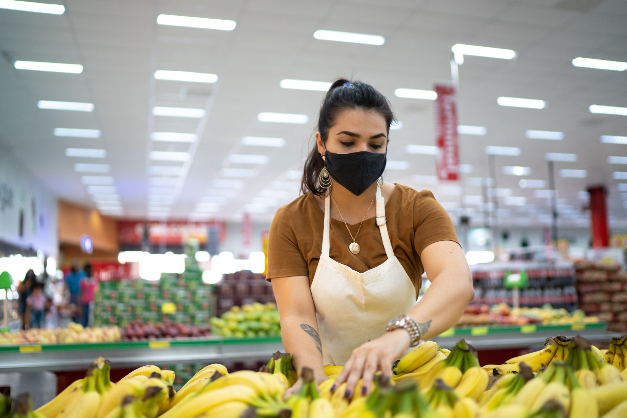 Young woman wearing face mask working in a supermarket arranging fruits