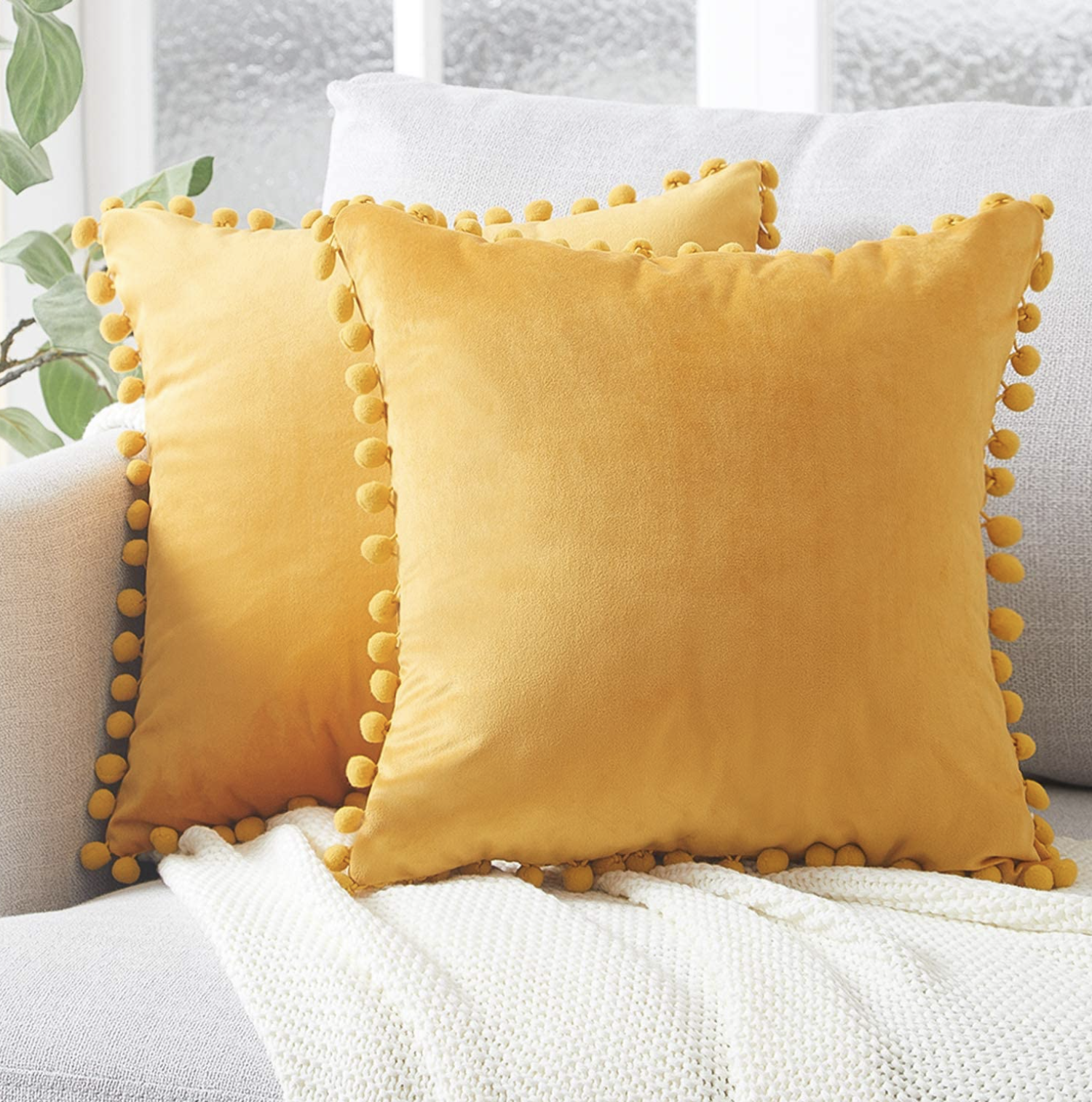 Two yellow colored throw pillows with pom pom borders