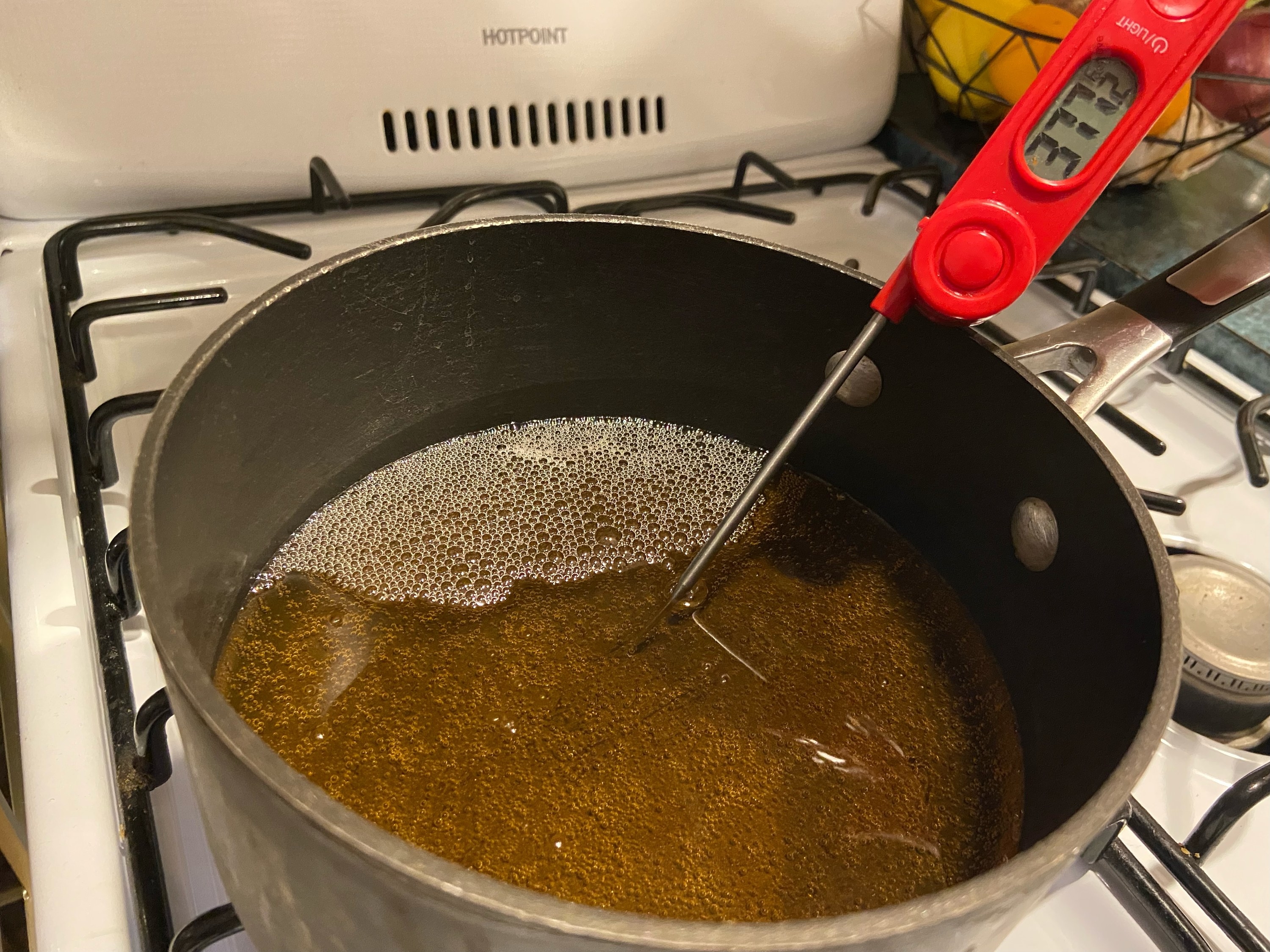 Someone using a meat thermometer to check the temperature of the oil.