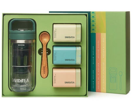 The matcha kit in the box with three tins of tea, a small wooden measuring spoon, and a glass tumbler.