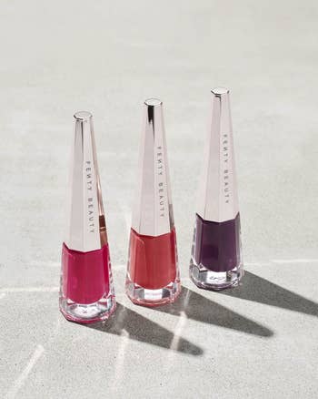 three bottles of fenty beauty lipstick with tall silver triangular lids