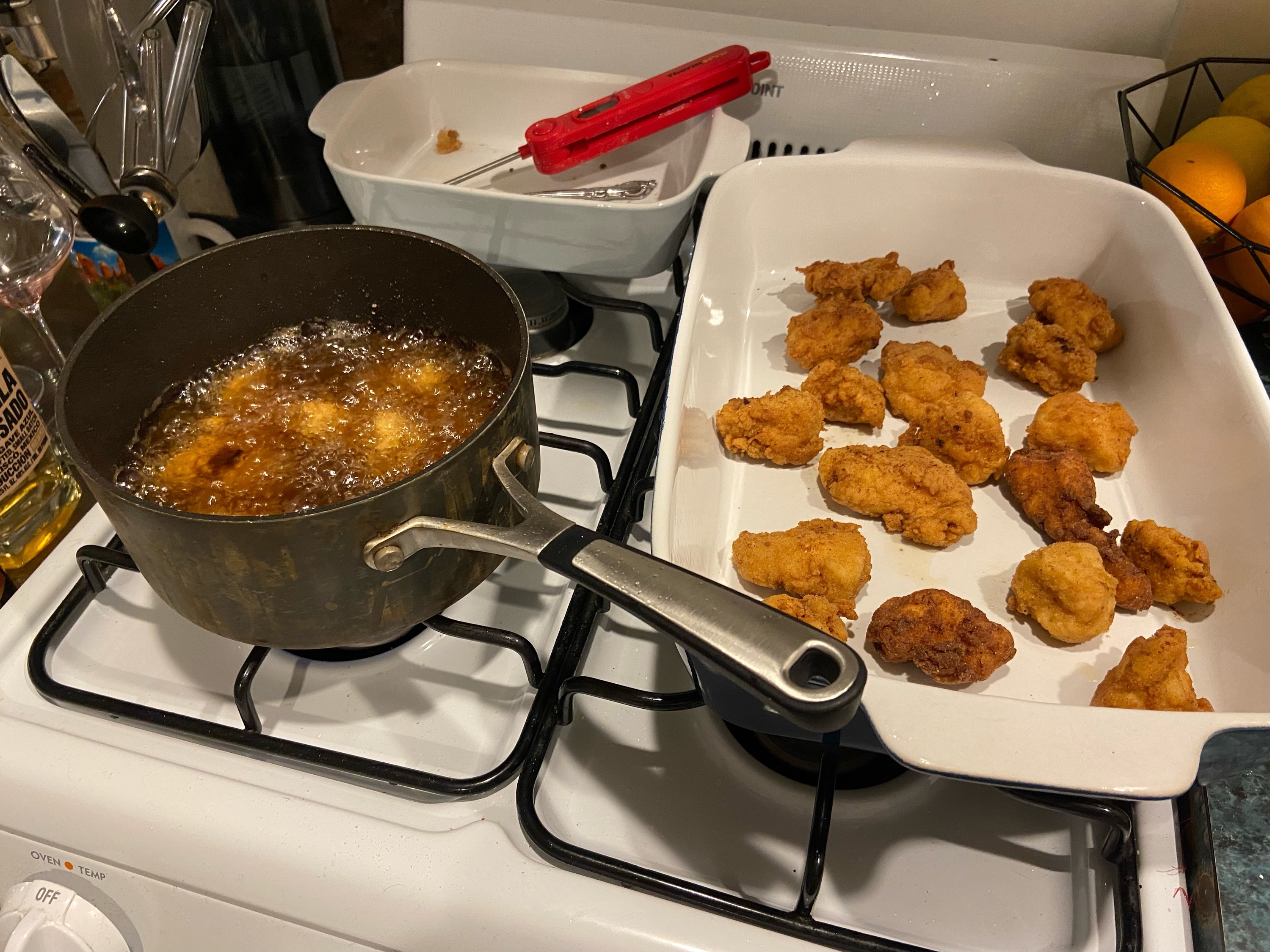 A serving dish with cooked chicken in it beside the frying pan as it cooks the final pieces.