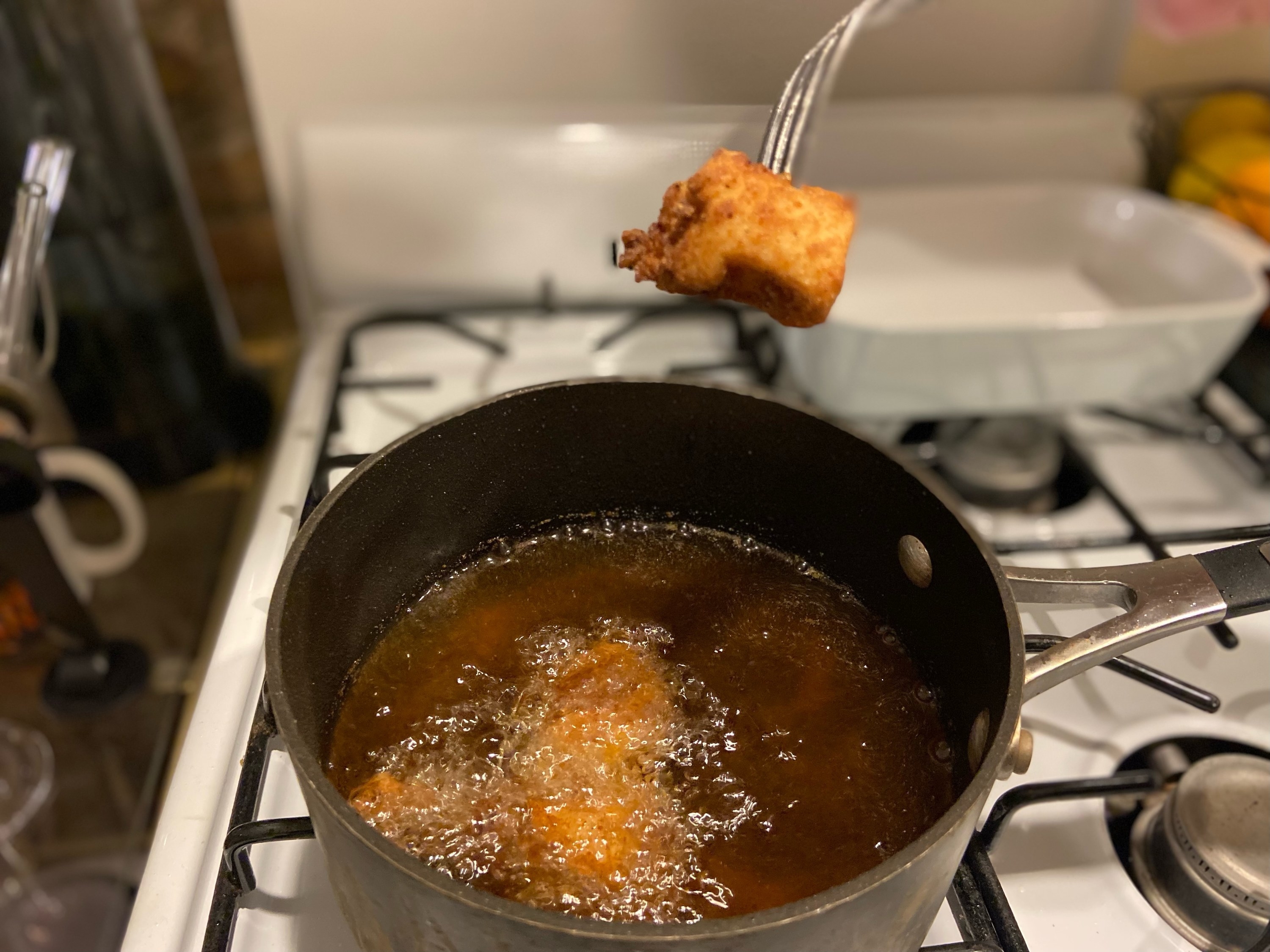 The first finished piece of chicken being pulled out of the oil.