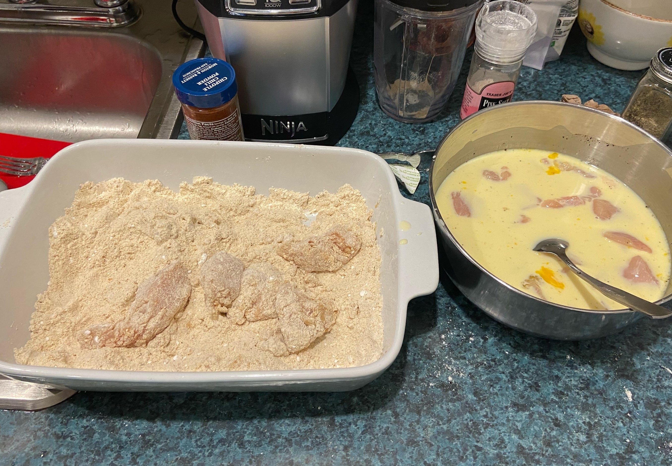 The chicken being coated in both the wet and dry ingredients.