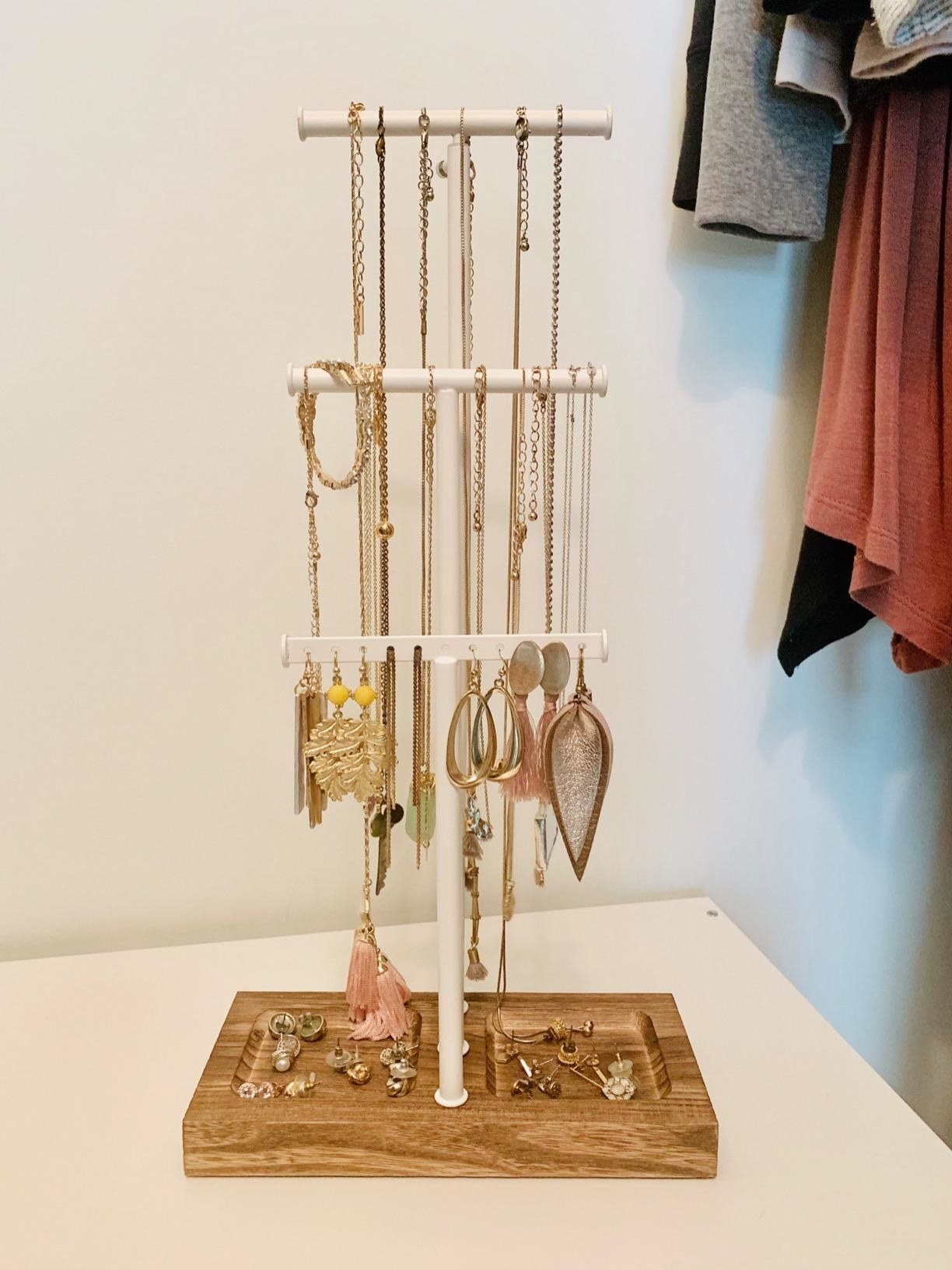 reviewer&#x27;s photo of their necklaces, bracelets, and earrings hung on the three-rung jewelry stand