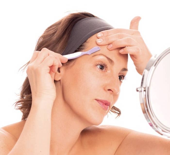 A model using a eyebrow shaping razor in front of a mirror