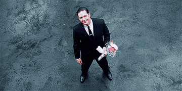 Tom Hardy as Reggie Kray smiles and holds out a bouquet of flowers