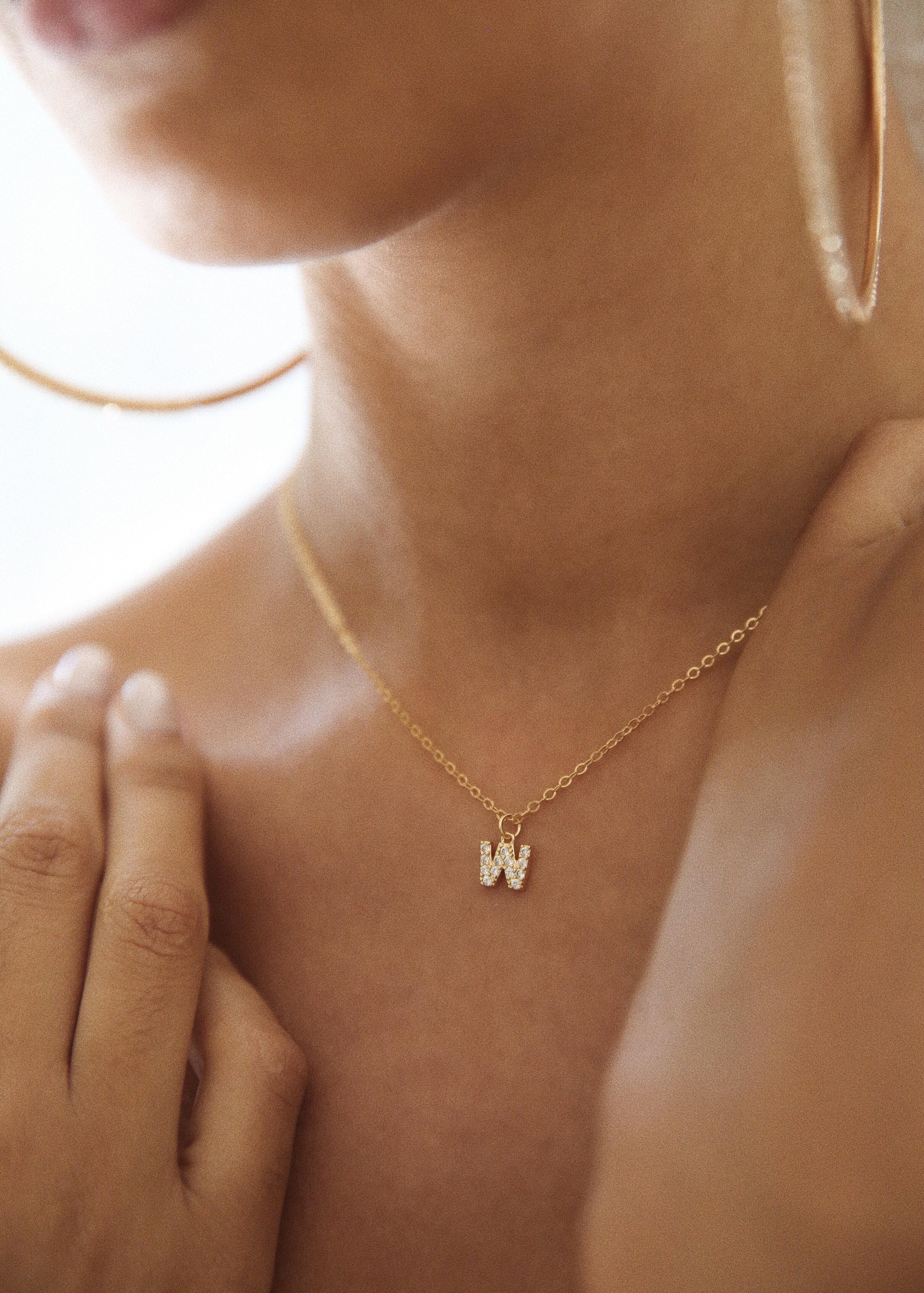 a model wearing a gold necklace with a &quot;w&quot; charm filled with crystals