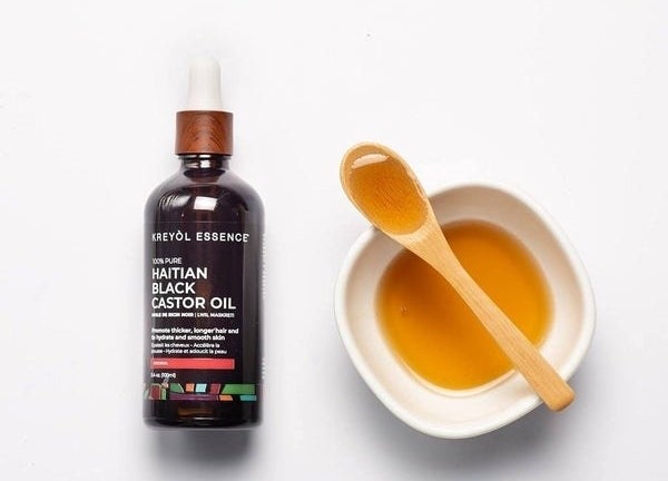 a dropper bottle of the castor oil next to a small bowl and wooden spoon filled with the oil