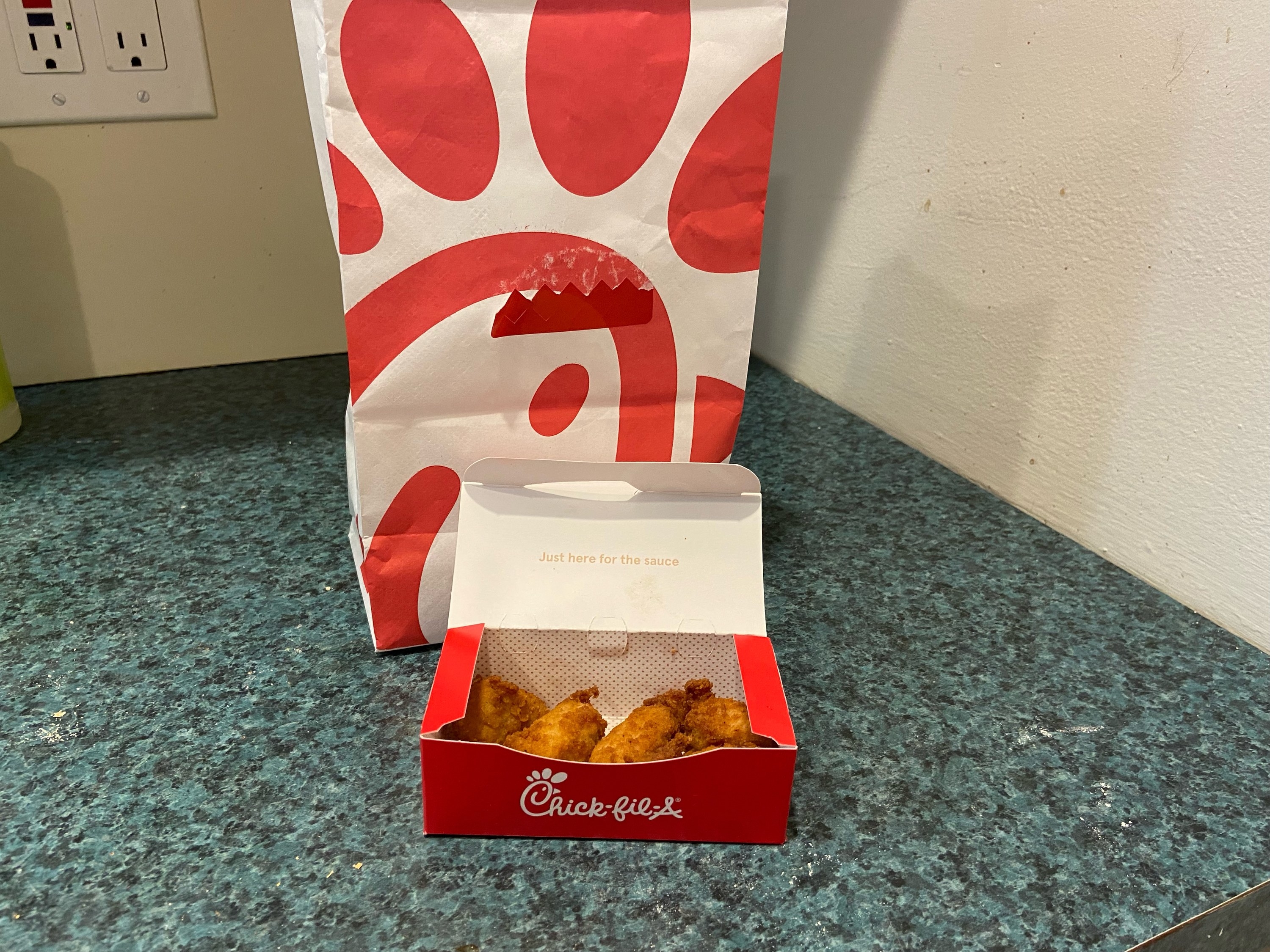 An order of Chick-Fil-A nuggets beside a to-go bag.