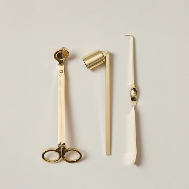 A wick trimmer, candle snuffer, and a wick dipper against a plain background