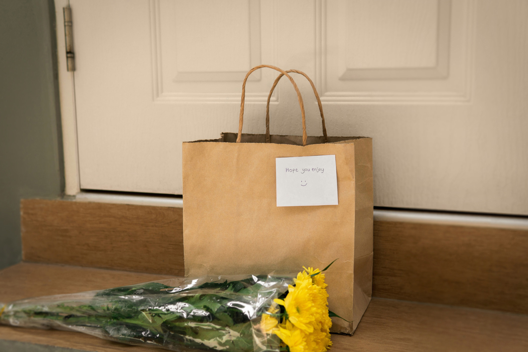 Bouquet of flowers and paper bag left outside of front door