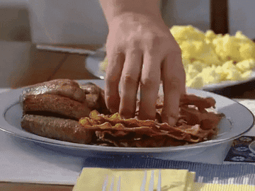 A hand reaching for bacon and putting in on a plate with eggs