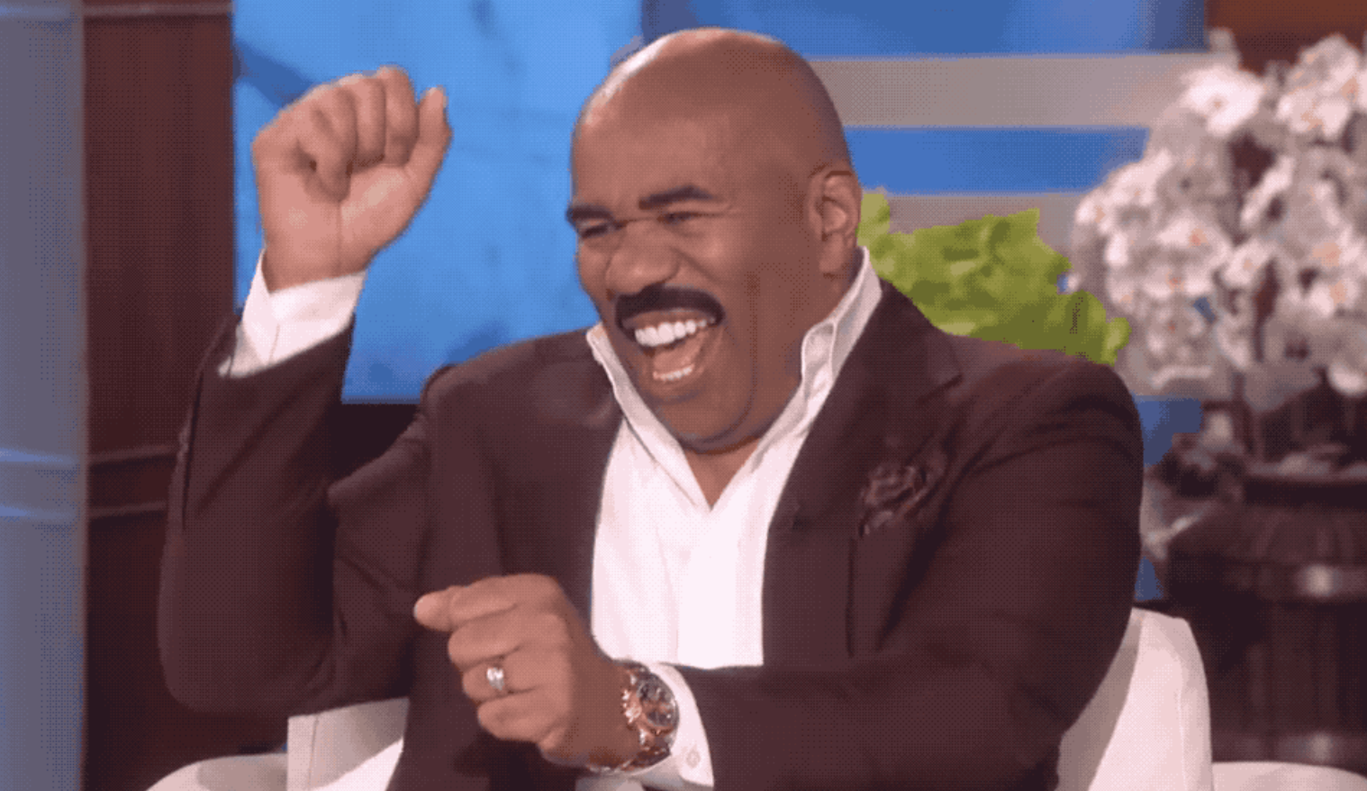 Steve Harvey smiling widely and raising his hands